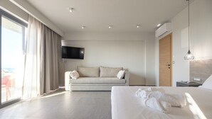 Une chambre d’hôtel moderne dotée d’un grand lit, d’un canapé, d’un téléviseur fixé au mur et d’une porte-fenêtre coulissante donnant sur l’extérieur.
