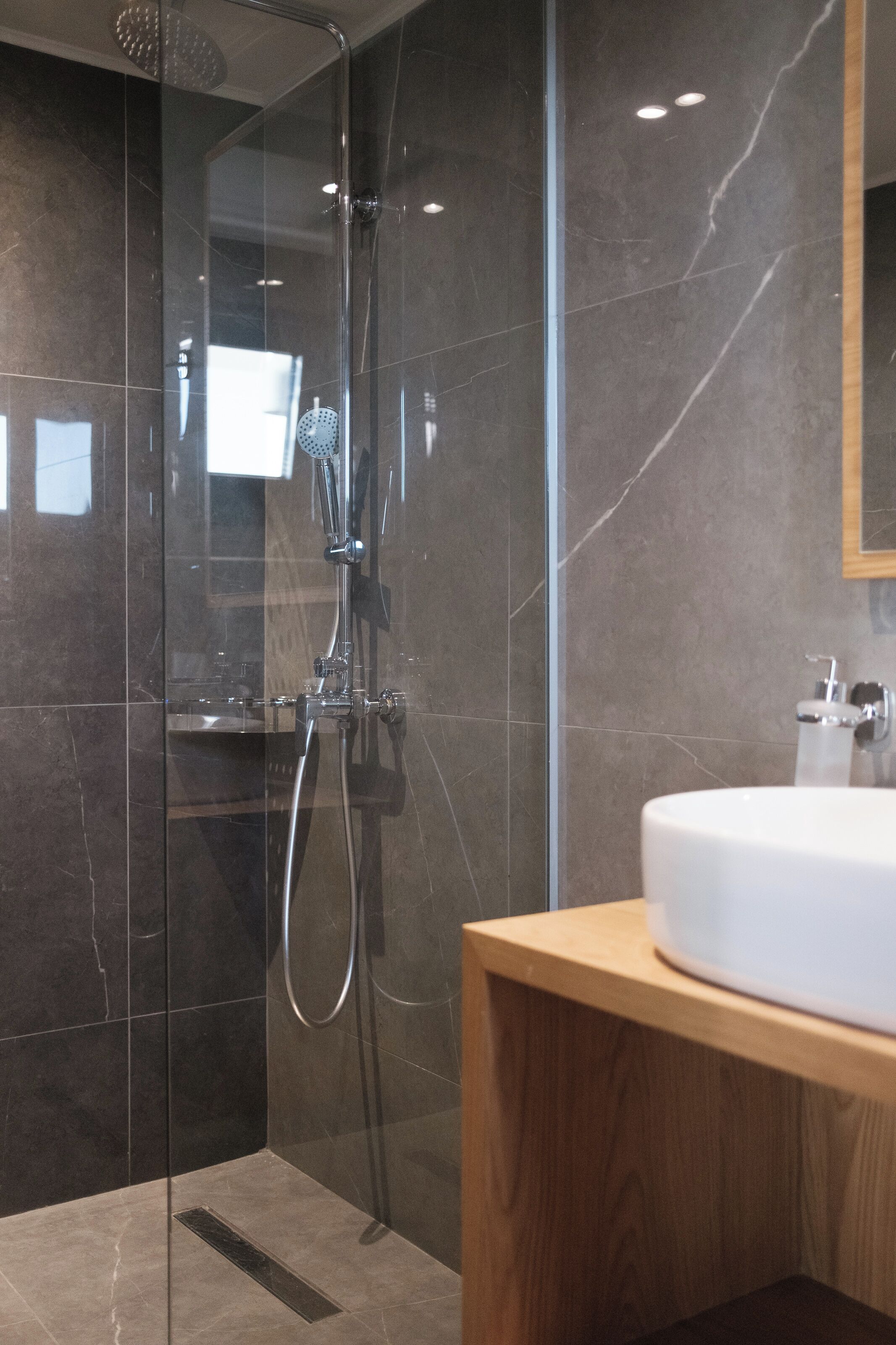 Un bany modern amb dutxa protegida per vidre, un moble de tocador de fusta i un lavabo blanc.
