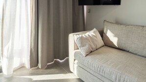 Un salon moderne avec un canapé, un téléviseur à écran plat fixé au mur et des rideaux légers.