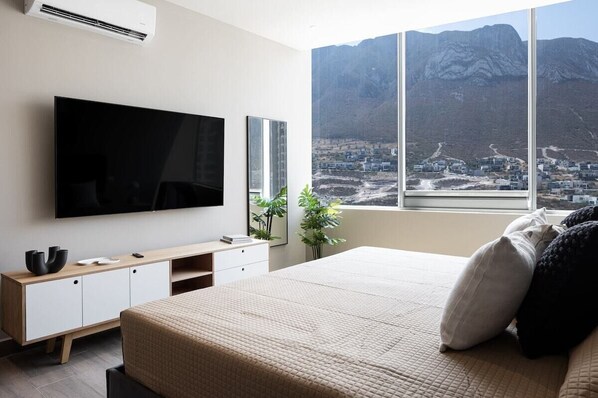 A bedroom with a large bed, a TV, a wooden cabinet, and a window with a mountain view. - Modern Apts w Pool & Mountain View (Santa Catarina)