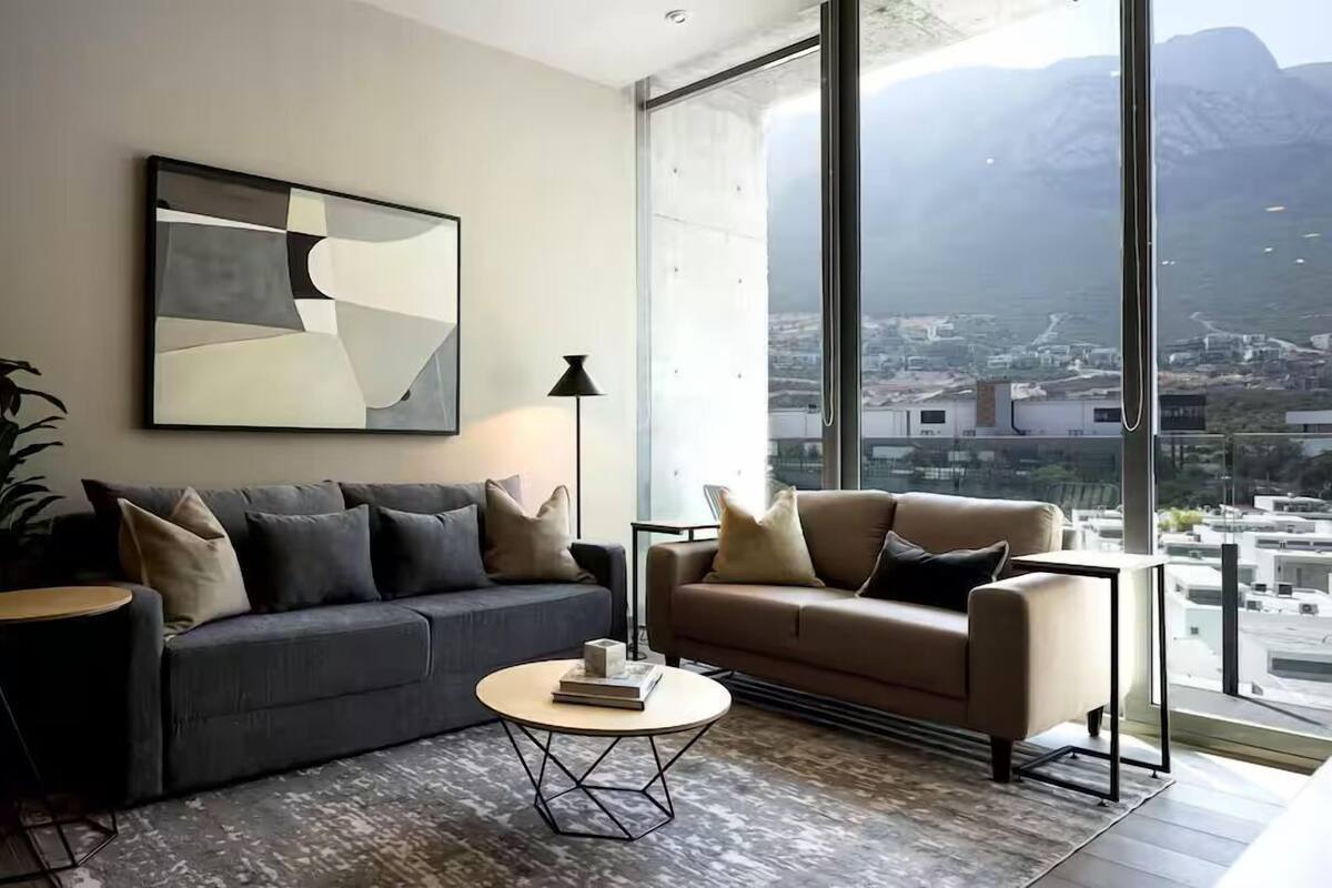 Una sala de estar moderna con dos sofás, una mesa de centro y un ventanal con vista a la ciudad.