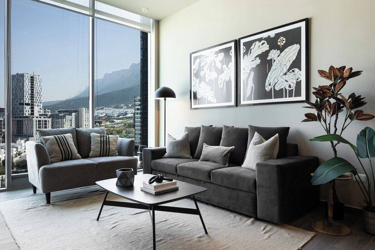 Una sala de estar moderna con un sofá gris, una mesa de centro y un ventanal con vistas a la ciudad.