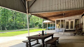 An outdoor covered picnic area with a concrete floor, wooden picnic tables, and benches.