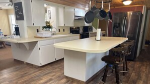 A modern kitchen with white cabinets, a central island with stools, a stainless steel refrigerator, and hanging pots.