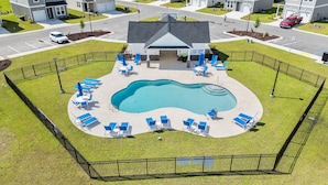 A swimming pool with lounge chairs and a covered area, surrounded by a fence.