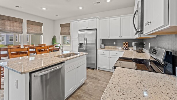 A modern kitchen with white cabinets, stainless steel appliances, granite countertops, and a dining area with wooden chairs.