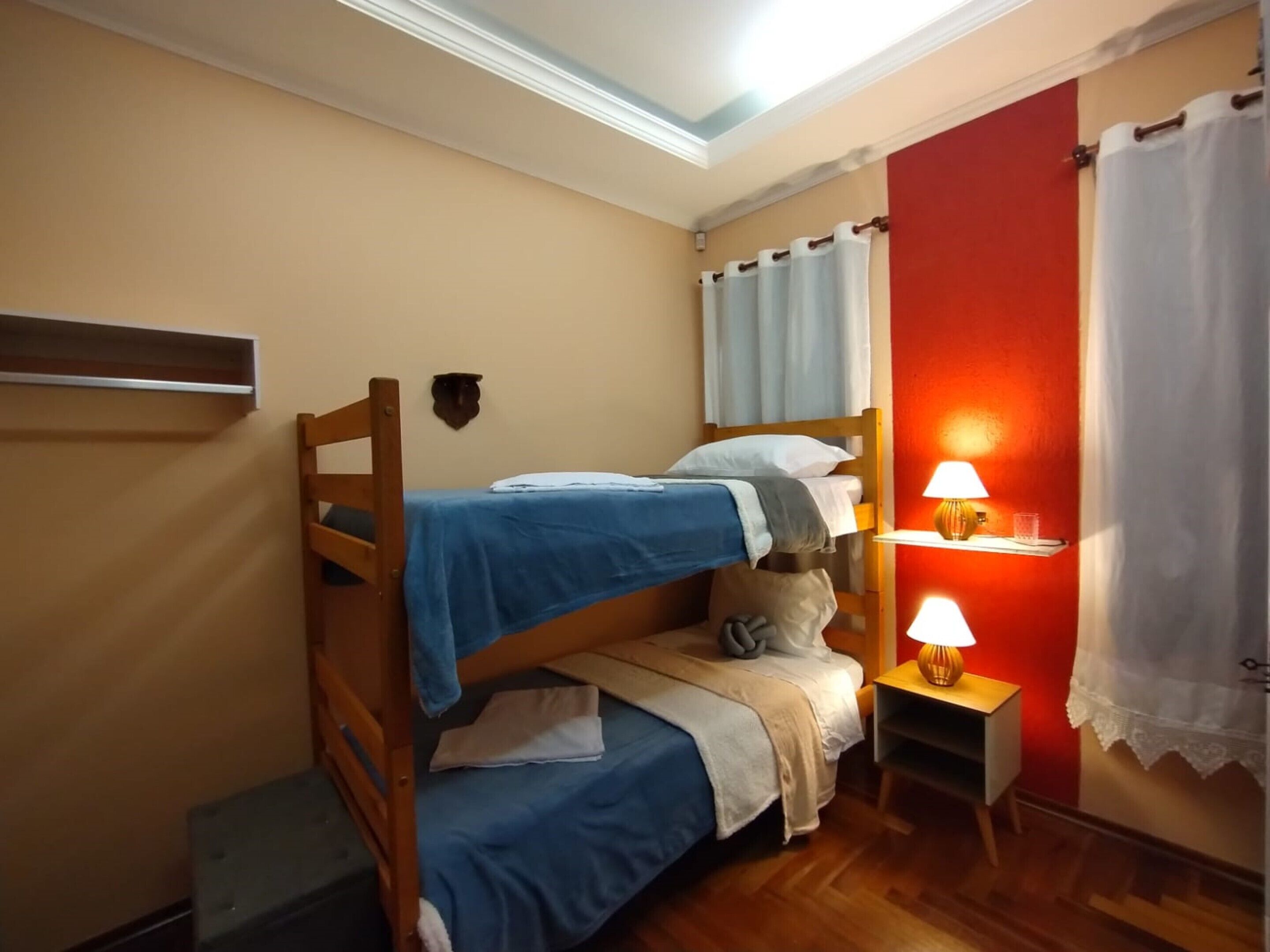 Habitación tipo dormitorio con dos literas, una mesita de noche pequeña con lámpara y una pared de acento roja.