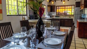 Un coin repas avec une table dressée pour quatre personnes, un vase avec une plante et, au fond, une cuisine.