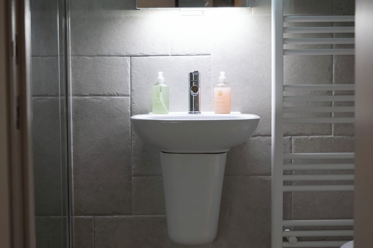 A bathroom with a white pedestal sink, a mirror above it, and two bottles of liquid soap on the sink.