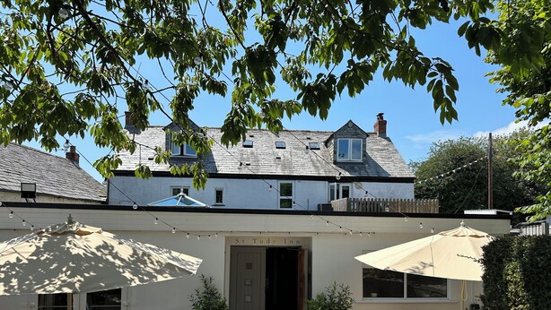 A building with a white facade, a wooden deck, outdoor seating, and potted plants. - St Tudy Inn (Bodmin)