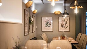 A dining area with a long table set for six, surrounded by upholstered chairs. There are framed botanical prints on the wall, and pendant lighting hangs above. - St Tudy Inn (Bodmin)