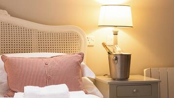A neatly made bed with a checkered pillow, a bedside lamp, and a bucket.