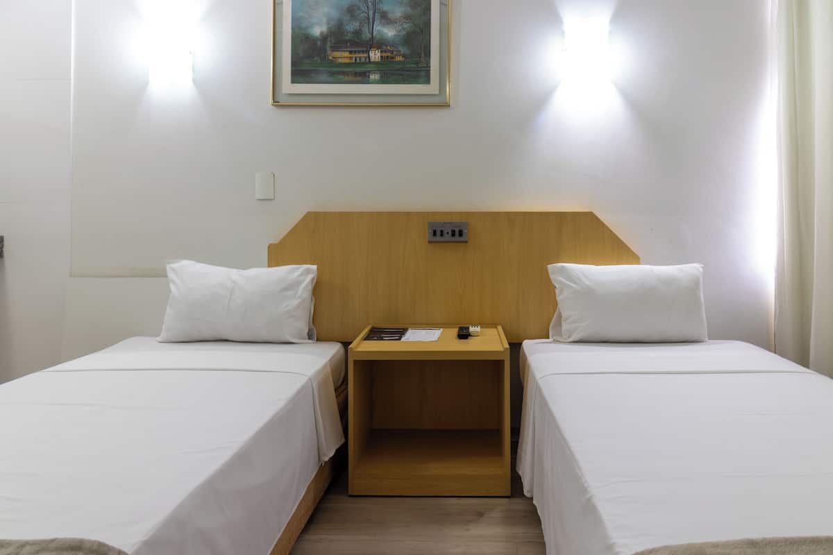 Ein Hotelzimmer mit zwei Einzelbetten, einem Holznachttisch dazwischen und einem Bild an der Wand.