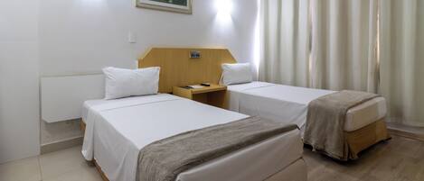 Habitación de hotel con dos camas, una mesita de noche, un cuadro en la pared y una ventana con cortinas.