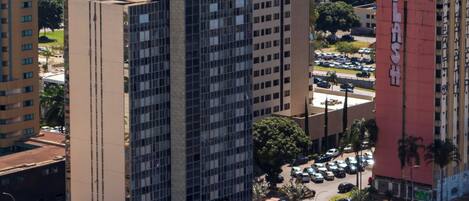 Un edificio alto con varios pisos, rodeado de otros edificios y una calle concurrida con coches y un autobús.