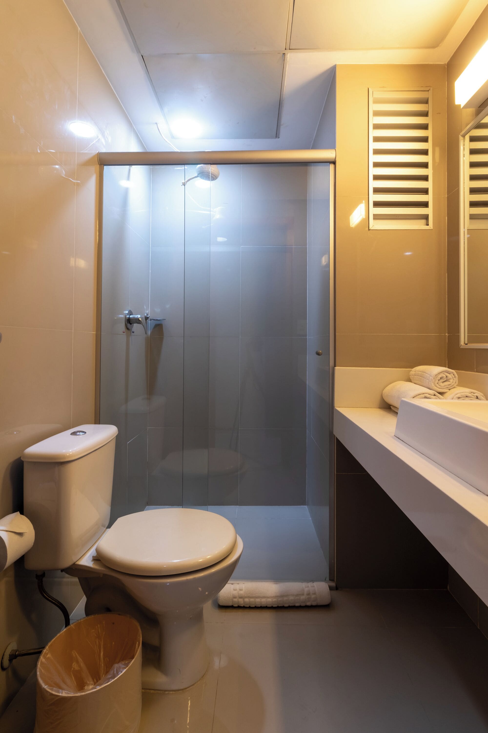 Un baño moderno con ducha envuelta en vidrio, inodoro y tocador con toallas.