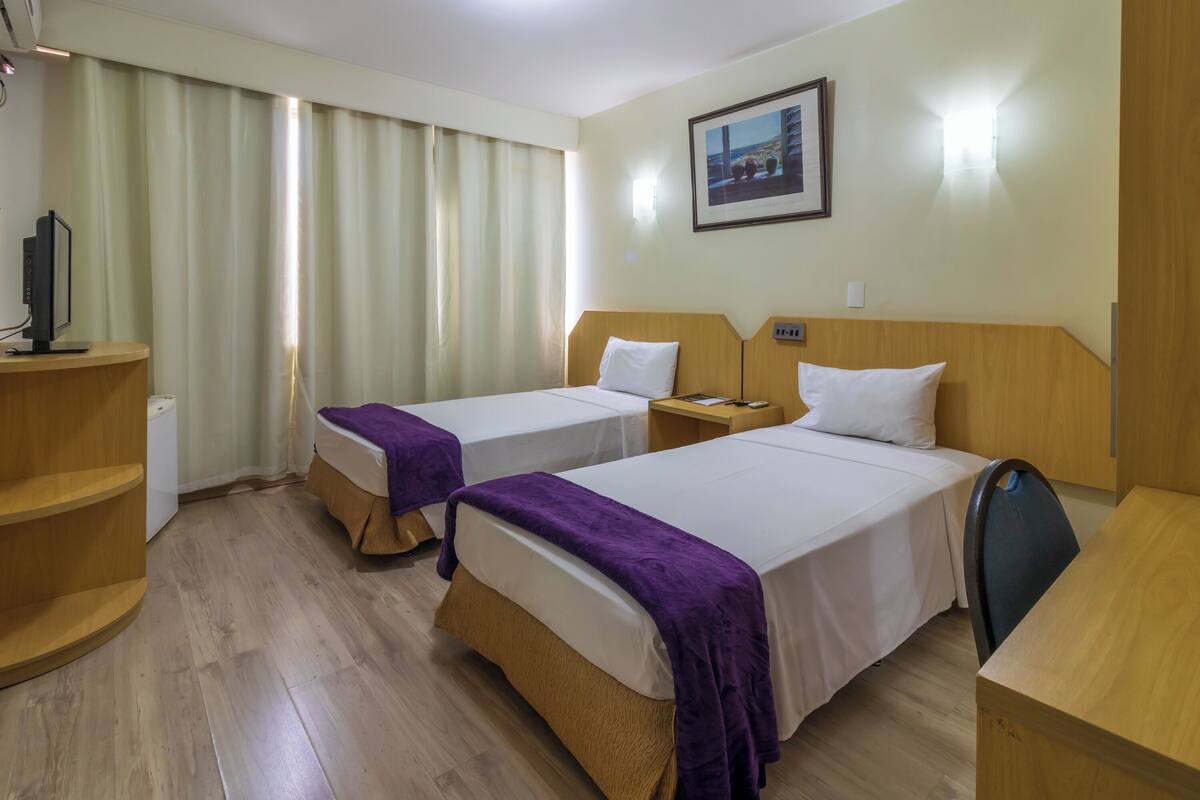 Ein Hotelzimmer mit zwei Betten, einem Schreibtisch, einem Stuhl, einem Fernseher und einem Bild an der Wand.
