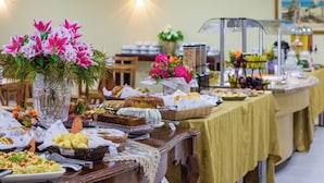 A buffet table with various food items and a vase of flowers. - Brasilia Tower Hotel by Castelo Itaipava (Brasília)