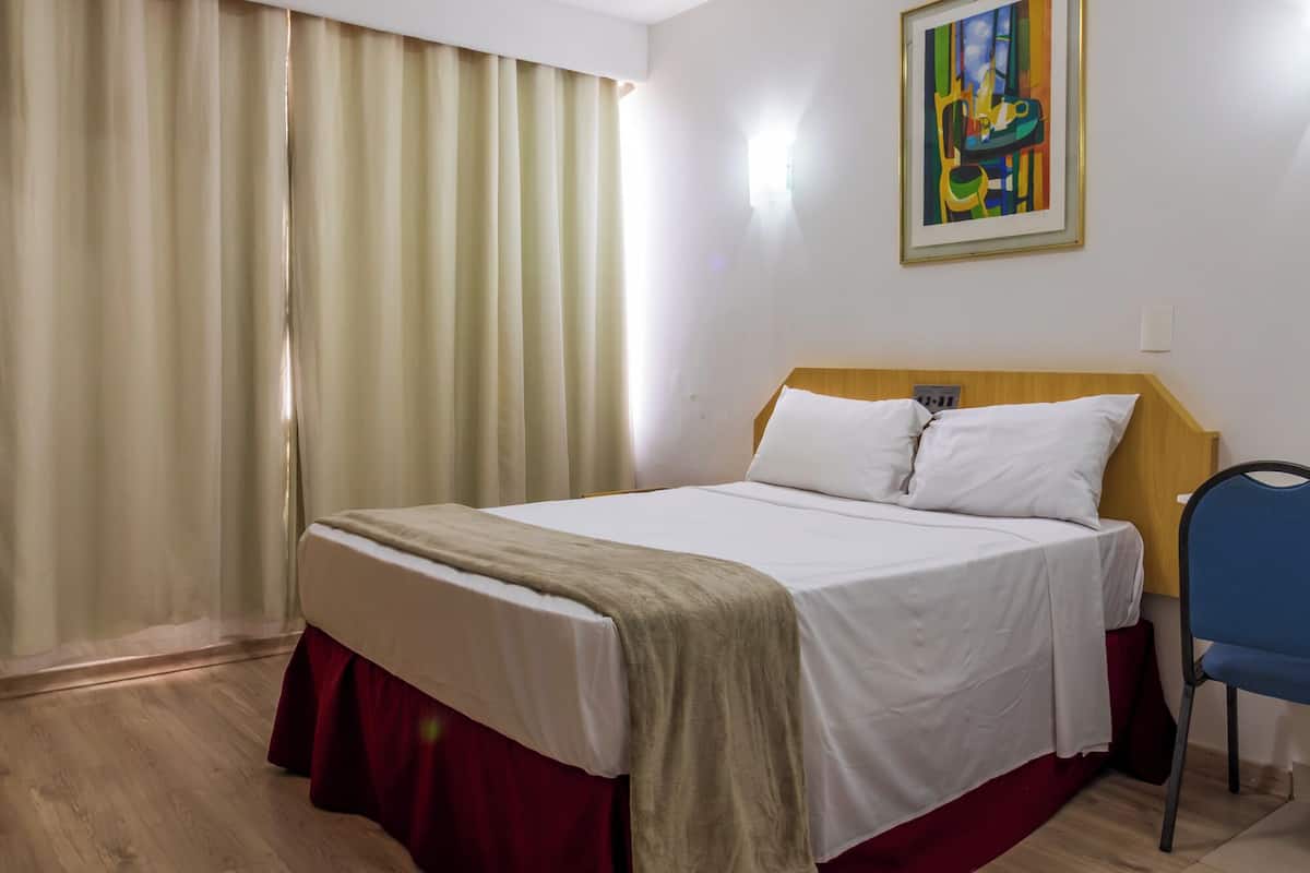 Ein Hotelzimmer mit einem Bett, einem Sessel, einem Bild an der Wand und einem Fenster mit Vorhängen.