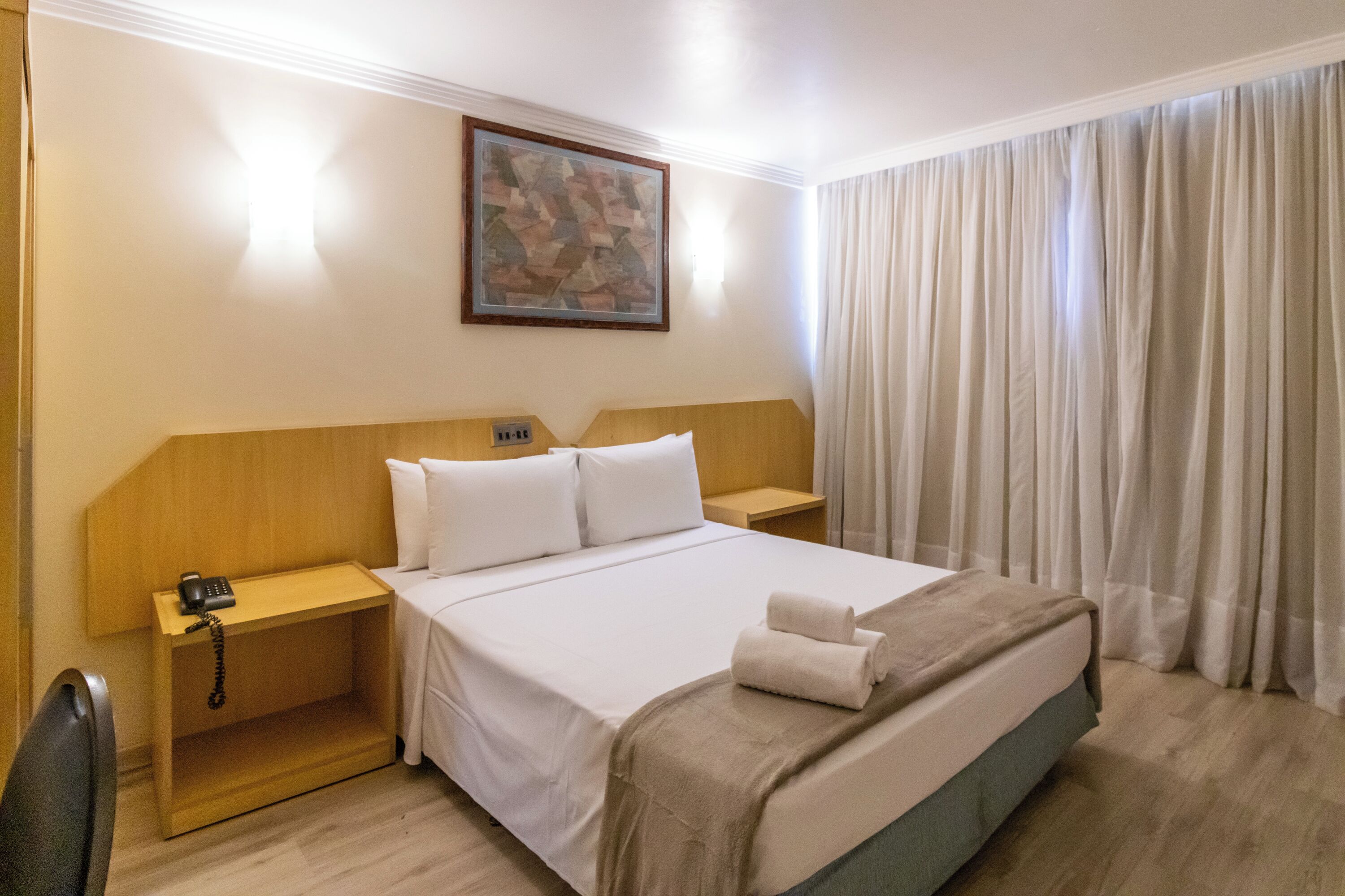 Camera d'albergo con un letto grande, una testiera in legno, un comodino con il telefono e un quadro appeso al muro.