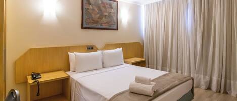 A hotel room with a large bed, a wooden headboard, a bedside table with a phone, and a painting on the wall.
