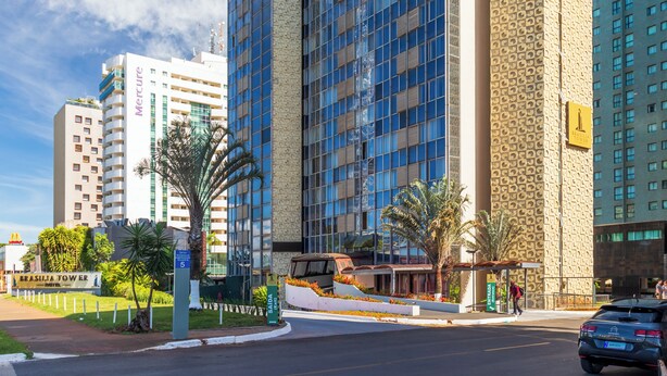 A modern high-rise building with a glass facade, surrounded by palm trees and a clear sky. - Brasilia Tower Hotel by Castelo Itaipava (Brasília)