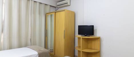 A hotel room with two single beds, a wardrobe, a television on a wooden stand, and an air conditioning unit.