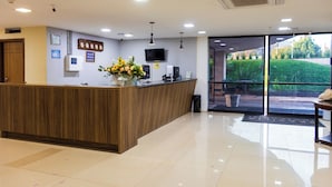 A reception area with a wooden reception desk, a flat-screen TV, and a wall-mounted clock. - Brasilia Tower Hotel by Castelo Itaipava (Brasília)