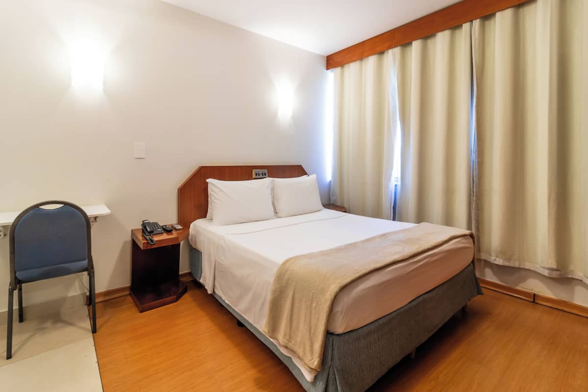 Ein Hotelzimmer mit einem Bett, einem Schreibtisch mit Telefon, einem Stuhl und einem Nachttisch.