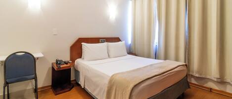 A hotel room with a bed, a desk with a telephone, a chair, and a nightstand.