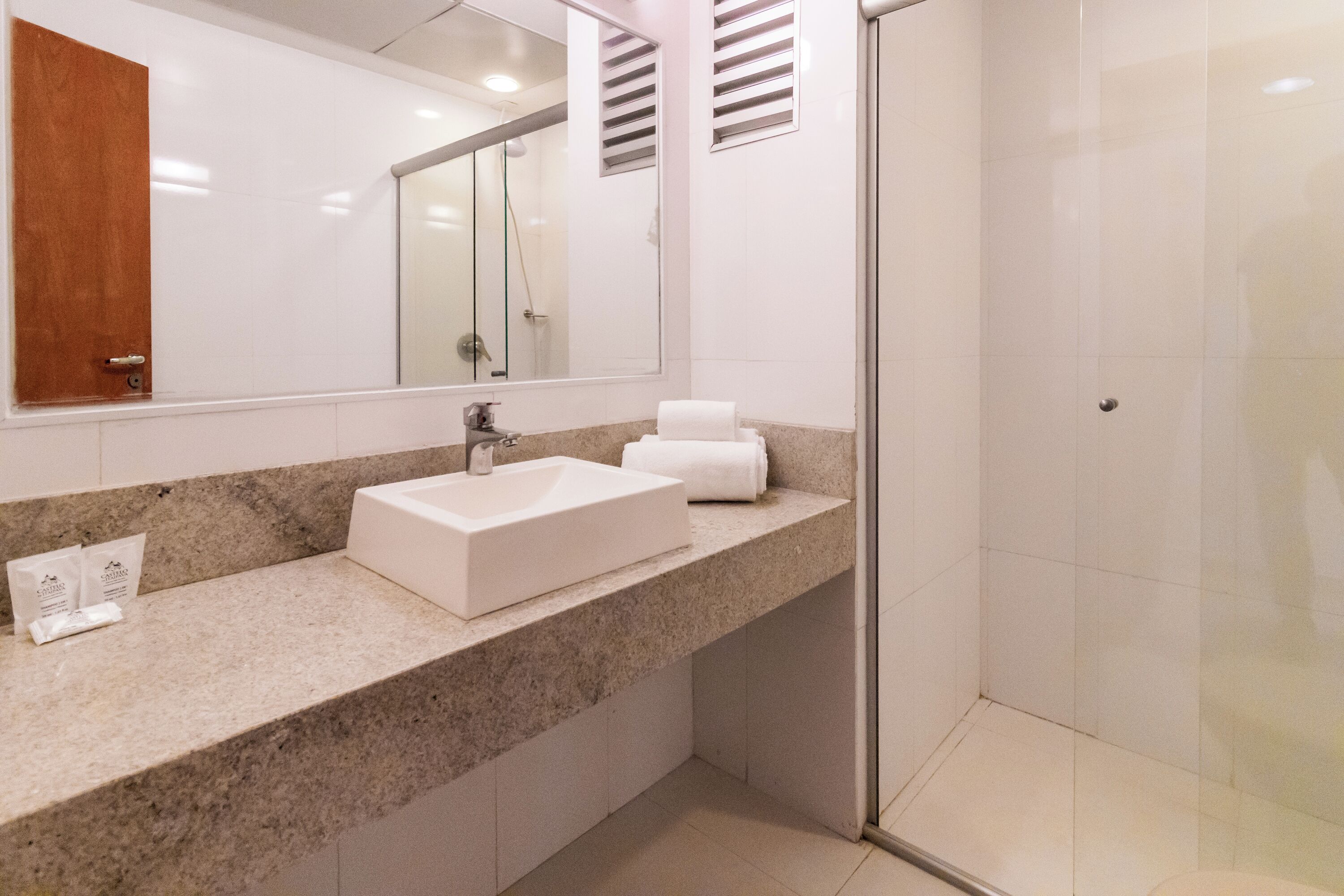 Un baño moderno con encimera de granito, lavabo blanco, espejo grande y cabina de ducha con paredes de vidrio.