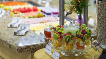 Buffet com diversos alimentos, incluindo frutas, legumes e um recipiente com granola.