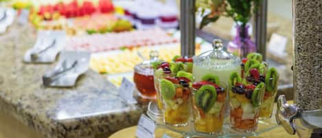 Un bufé con diversos alimentos, entre ellos frutas, verduras y un recipiente con granola.