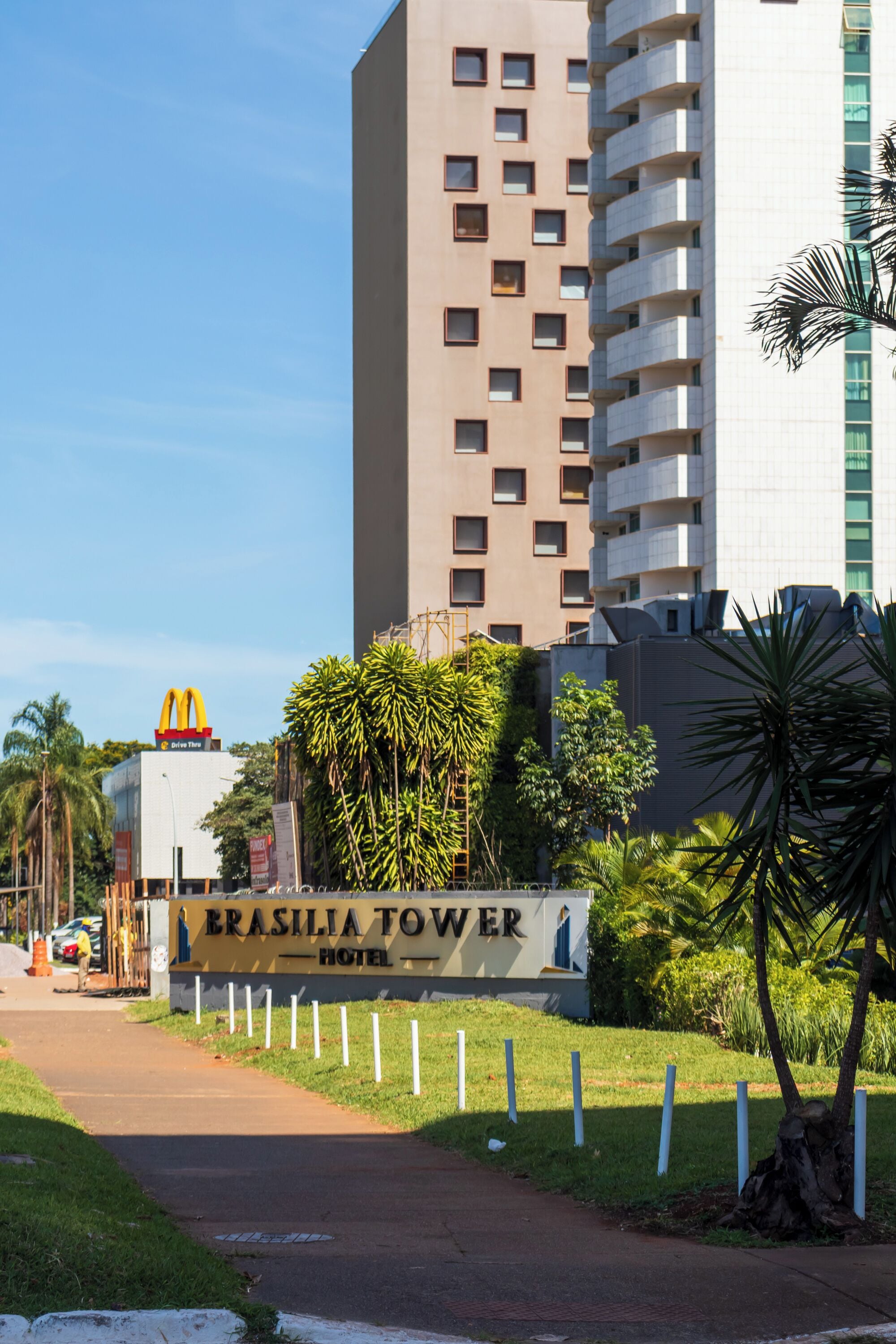 L’entrée d’un hôtel, avec une enseigne indiquant « Brasilia Tower Hotel », est entourée de verdure et se trouve devant un grand immeuble.