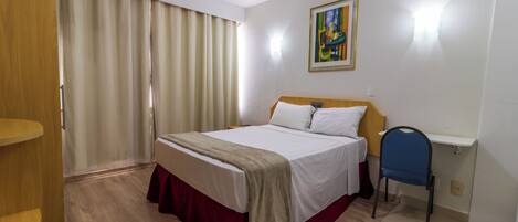Une chambre d’hôtel avec un lit, un bureau, une chaise, une armoire et un tableau au mur.
