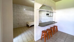 A compact kitchen with a microwave, a bench, and a bar area with stools. - AP 04 Ala Morrinhos Residencial Solavir (Bombinhas)