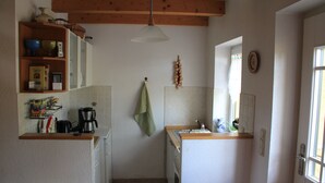 Cocina compacta con armarios blancos, encimera de madera, lámpara colgante y ventana con cortinas.