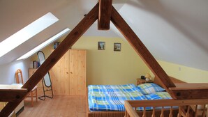 Un dormitorio con techo inclinado, vigas de madera, una cama con colcha escocesa, una mesita de noche, una silla y un armario de madera.
