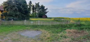 A rural landscape with a wooden fence, a swing set, and a field of yellow flowers.