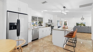 A modern kitchen with white cabinets, stainless steel appliances, and a central island with bar stools. - Labor Day Sale: Gulf Access, Hot Tub, Kayaks, Fishing & Pet Friendly (North Fort Myers)
