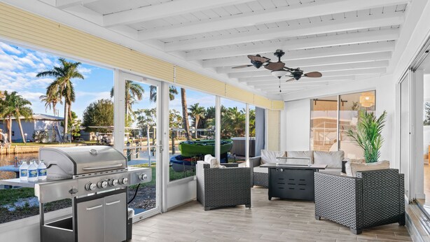 A covered outdoor patio with a grill, seating area, and large windows overlooking a pool and palm trees. - Labor Day Sale: Gulf Access, Hot Tub, Kayaks, Fishing & Pet Friendly (North Fort Myers)