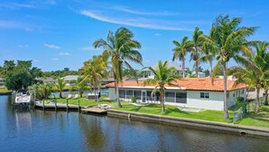 A waterfront property with a dock, palm trees, and a house with a red-tiled roof. - Labor Day Sale: Gulf Access, Hot Tub, Kayaks, Fishing & Pet Friendly (North Fort Myers)