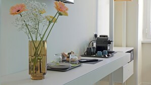 A hotel room with a desk, a coffee maker, a vase with flowers, and a hanging coat rack. - Domus Augustea San Giovanni Sunset Suites - Deluxe Suite Ottanivm (Roma)