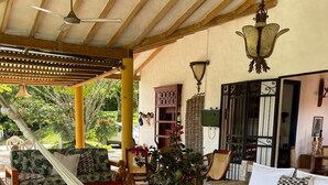 Un espacio al aire libre techado con mobiliario de mimbre, una hamaca y una planta en maceta.