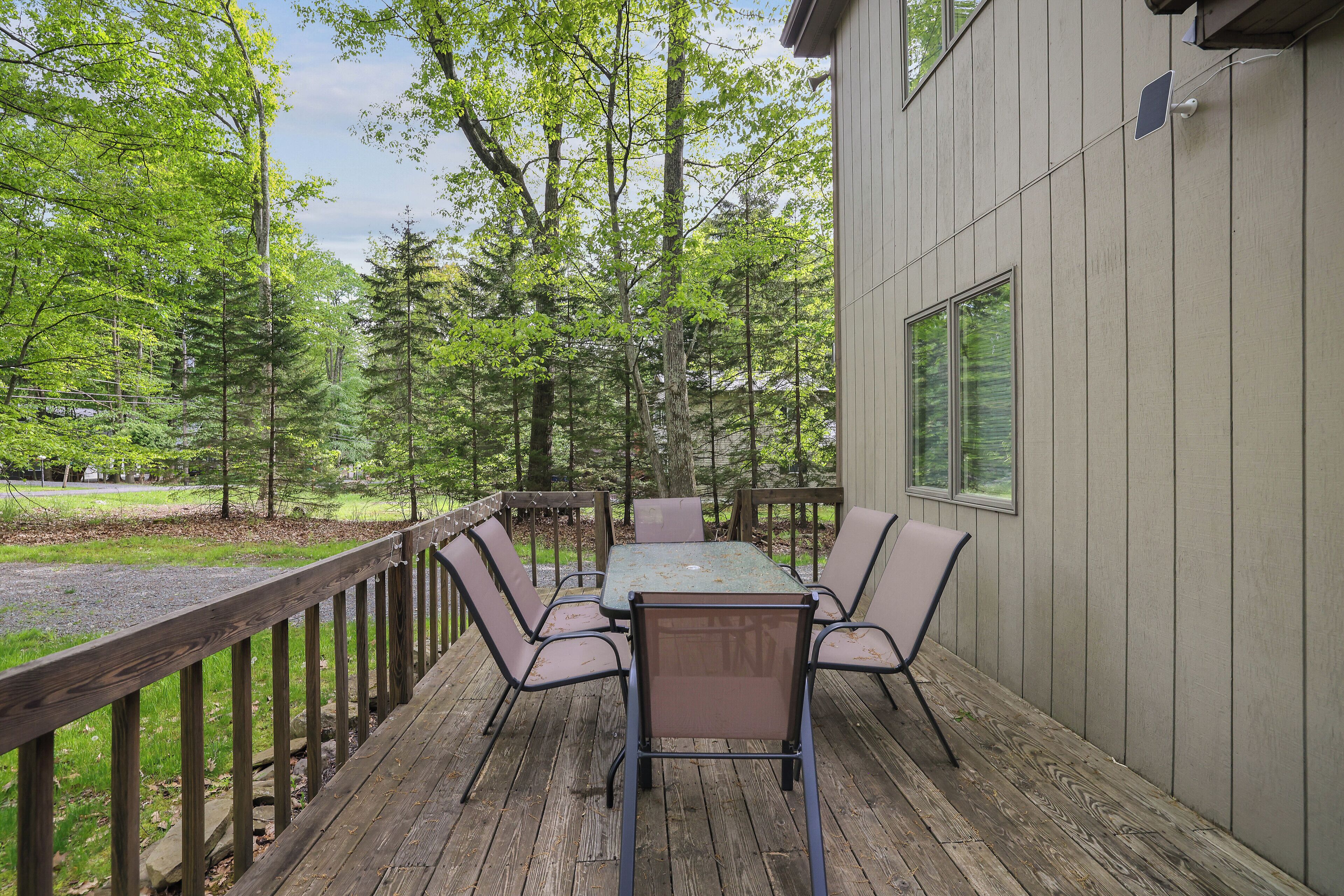 A deck with a table and chairs, surrounded by a wooden railing, overlooking a forested area.