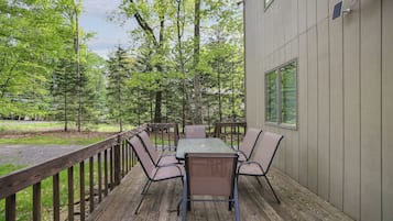 A deck with a table and chairs, surrounded by a wooden railing, overlooking a forested area.