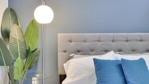 A bedroom with a tufted headboard, a bedside lamp, and a potted plant.