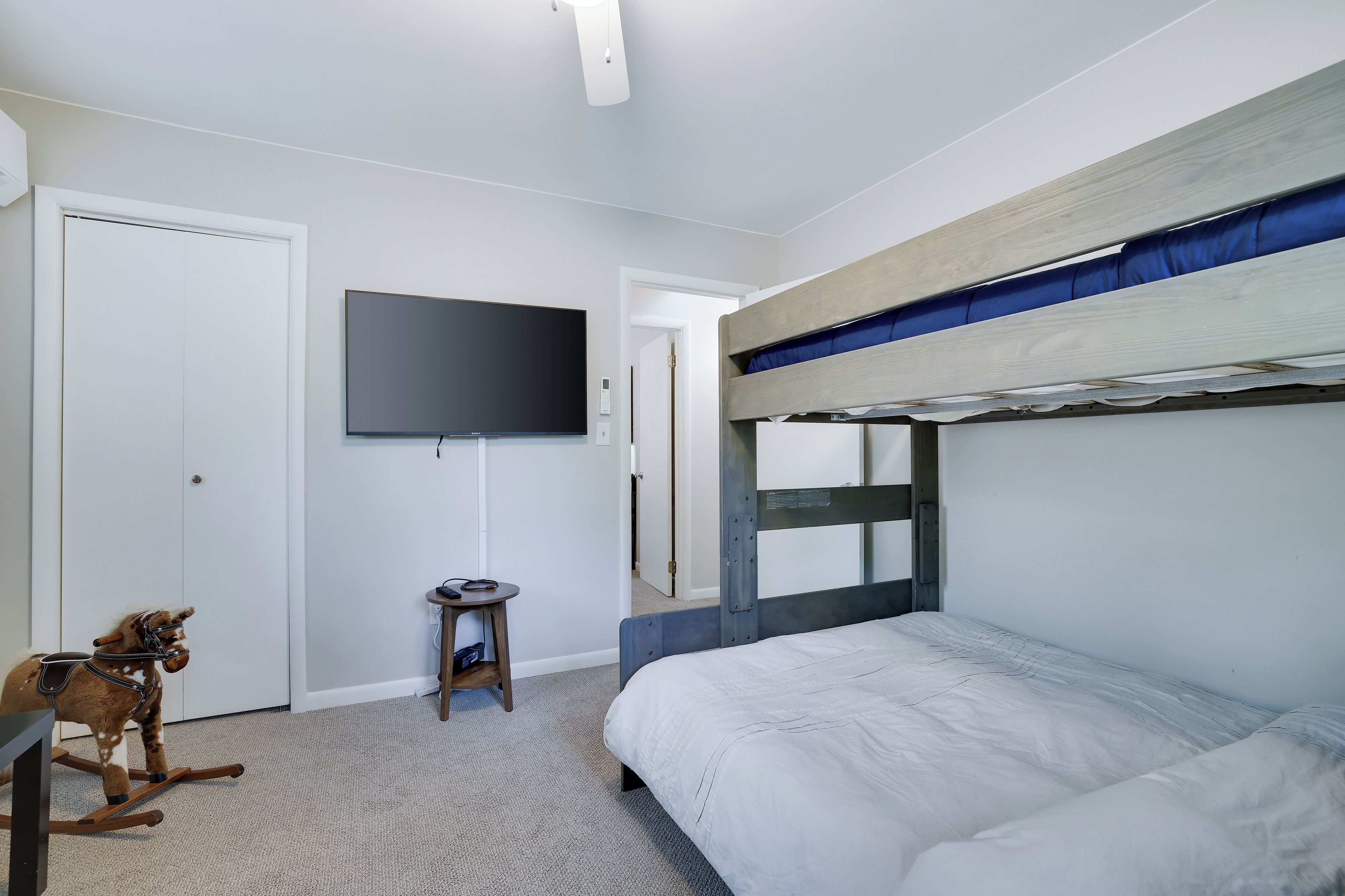 A bedroom with a bunk bed, a television mounted on the wall, a small table with a chair, and a rocking horse.