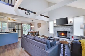 Amplia sala de estar con chimenea, un sofá grande, una mesa de comedor y una cocina con una isla azul.