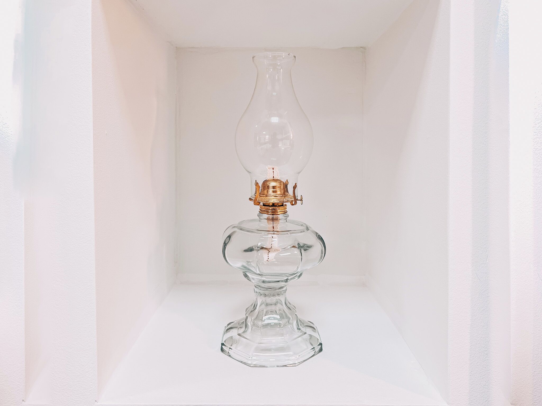 A clear glass lamp with a gold base, placed in a white shelf.